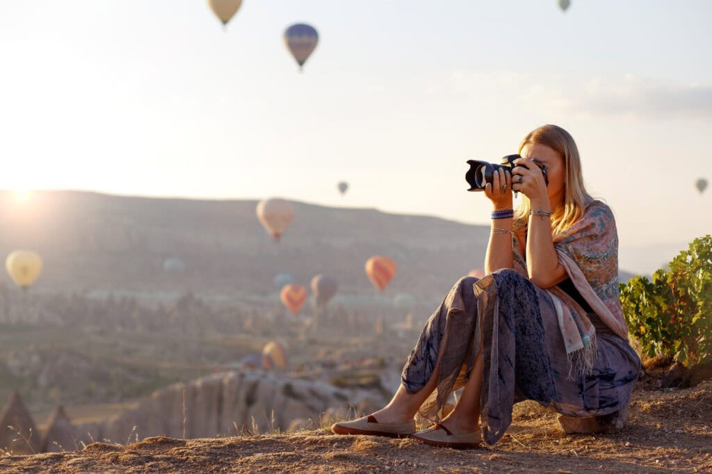 woman holding camera and taking pictures of hot air balloons for article how to make $20,000 a month as a photographer