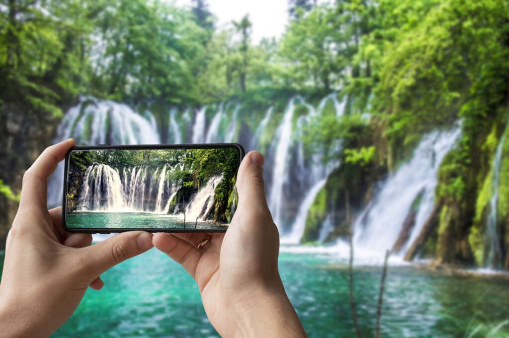 picture of someone holding their phone and taking a picture of a waterfall. How To Make Money as a Travel Photographer