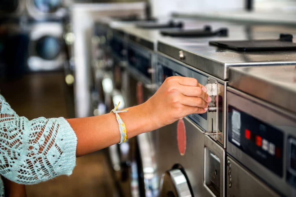 Picture of person putting coin in washer and dryer machine. Are laundromats profitable? 